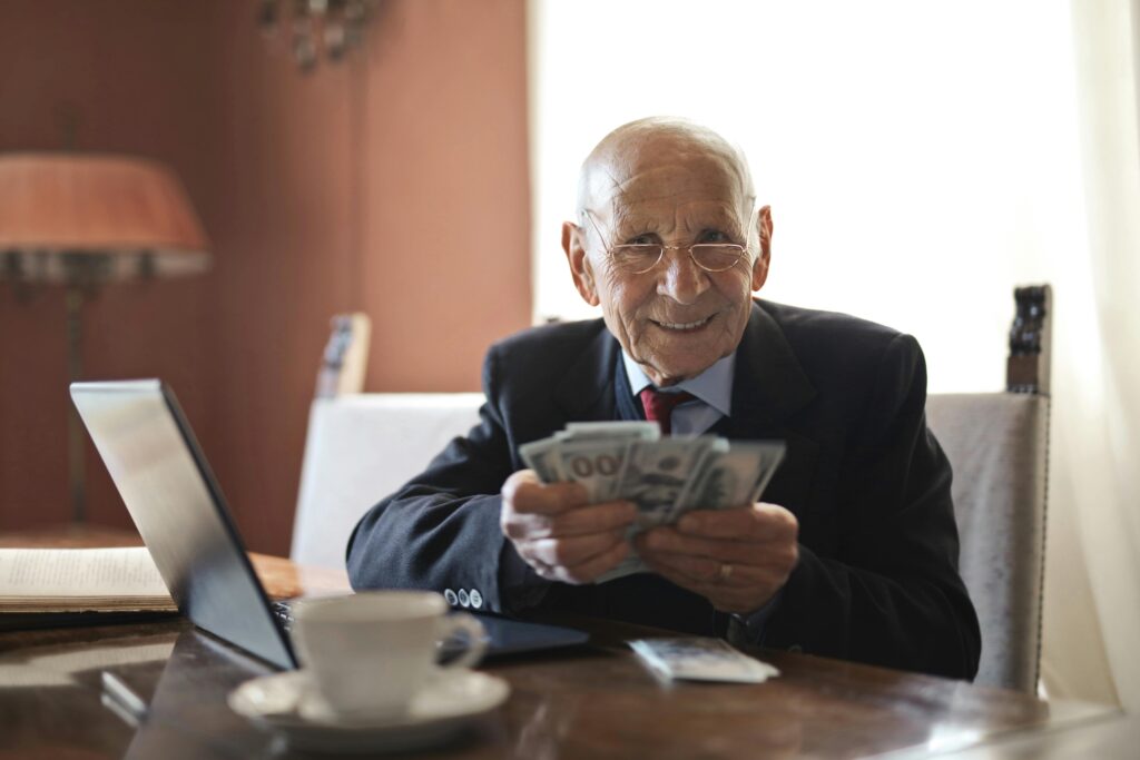 Elderly man smiling while counting cash at a home office setting.